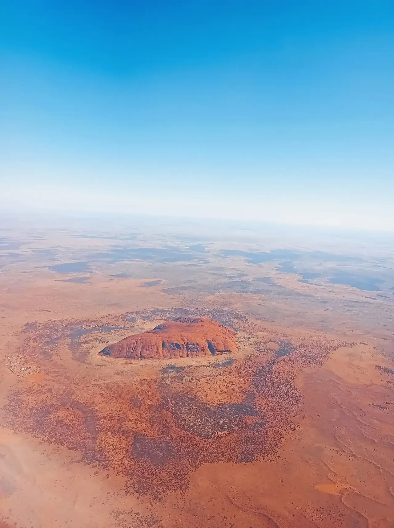 Uluru from high altitude, a lone dome on the flat red plain of central Australia